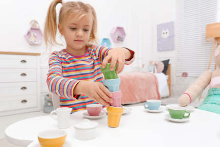 Cute little girl playing tea party at table in bedroomの写真素材