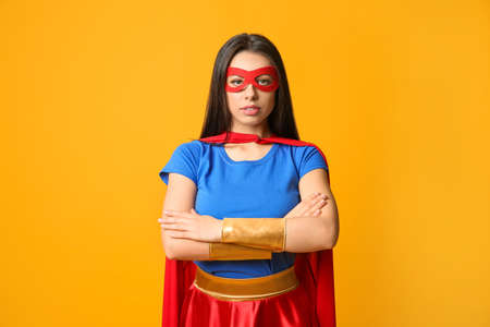 Confident young woman wearing superhero costume on orange backgroundの写真素材