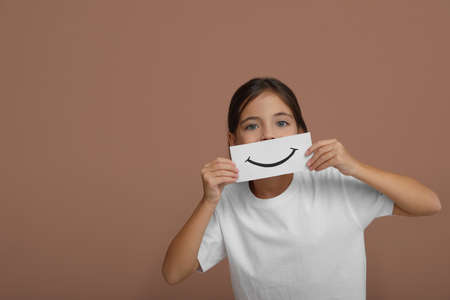 Little girl holding sheet of paper with smile on pale pink background, space for textの写真素材