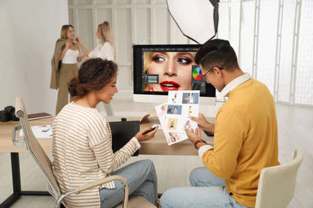 Professional retoucher with colleague working at desk in photo studio
