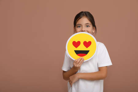 Little girl holding face with heart eyes emoji on pale pink background, space for textの写真素材