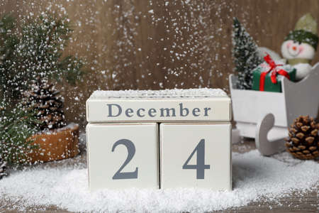 December 24 - Christmas Eve. Snow falling onto wooden block calendar and festive decor on tableの写真素材