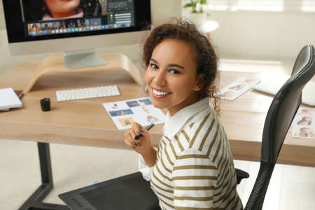 Professional African American retoucher working with graphic tablet at desk in office