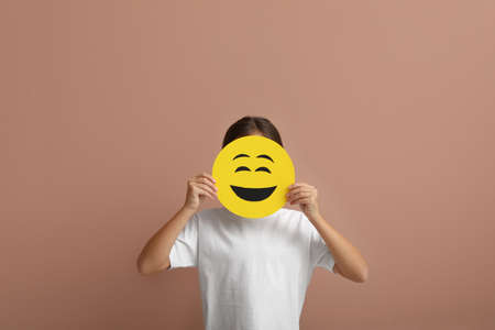 Little girl covering face with laughing emoji on pale pink backgroundの写真素材