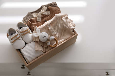 Wooden crate with children's clothes, shoes and toy on chest of drawersの写真素材