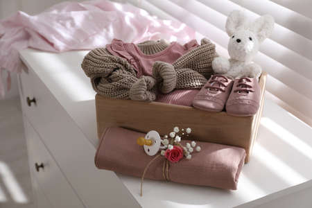 Wooden crate with children's clothes, shoes, toy and pacifier on chest of drawers in roomの写真素材