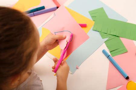 Little girl cutting color paper with scissors at table, above viewの写真素材