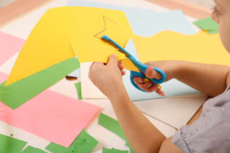 Little girl cutting color paper with scissors at table, closeupの写真素材