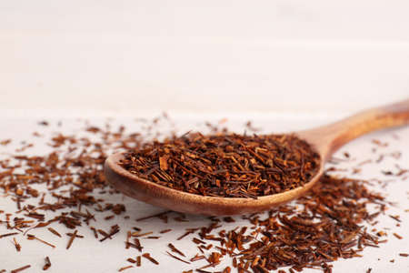 Spoon with dry rooibos tea leaves on white wooden table, closeupの写真素材