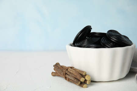 Tasty black candies and dried sticks of liquorice root on white table. Space for textの写真素材