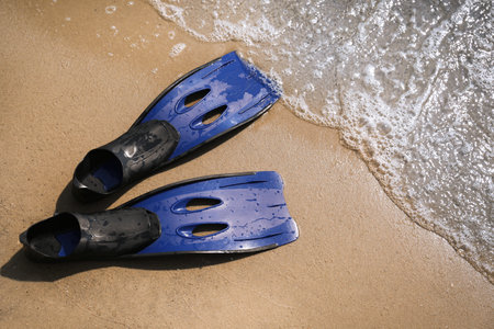 Pair of blue flippers on sand near sea, top viewの写真素材