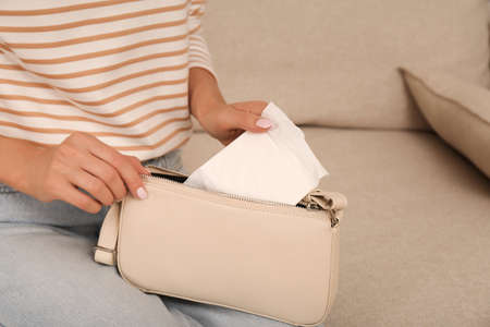 Woman putting disposable menstrual pad into purse at home, closeup