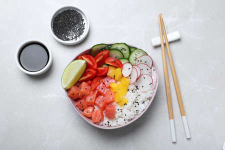 Delicious poke bowl with salmon, rice and vegetables served on light gray table, flat layの写真素材