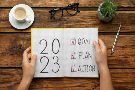 Woman holding notebook with text 2023 Goal, Plan, Action at wooden table, top view. New Year resolutionsの写真素材