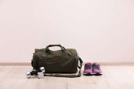 Green sports bag, sneakers and dumbbells on floor near white wall, space for textの写真素材