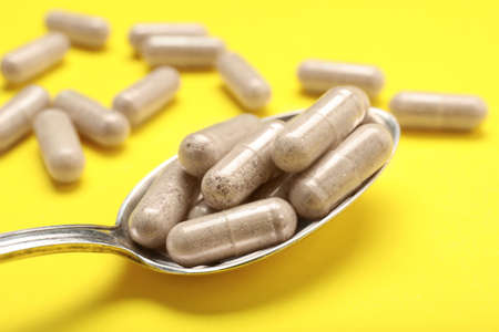 Gelatin capsules in spoon on yellow background, closeup