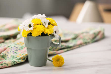 Beautiful bright flowers in cup and fabric on white marble table, space for textの写真素材