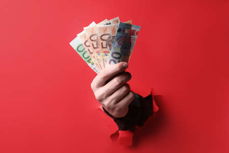 Businessman breaking through red paper with money in hand, closeup