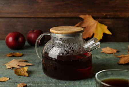 Glass teapot of hot beverage and autumn leaves on light blue wooden tableの写真素材