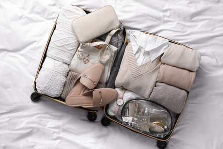 Open suitcase with folded clothes, shoes and accessories on bed, top viewの写真素材