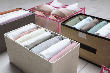 Different cases and organizer with folded clothes on white wooden background, closeup. Vertical...