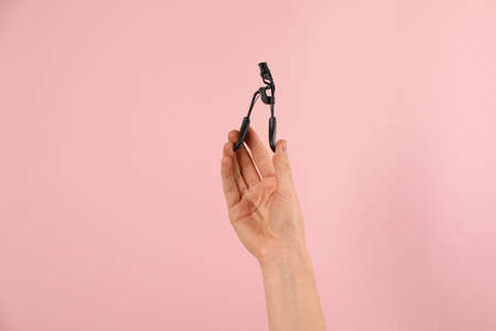 Woman holding eyelash curler on pink background, closeup. Makeup tool