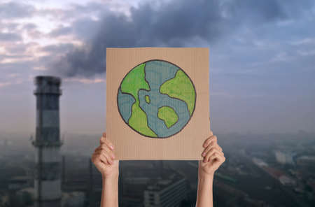 Protestor holding placard with Earth drawing and blurred view of industrial factory on background. Climate strikeの写真素材