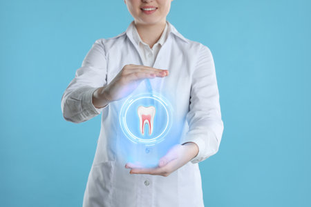 Dentist showing virtual model of tooth on light blue background, closeupの写真素材