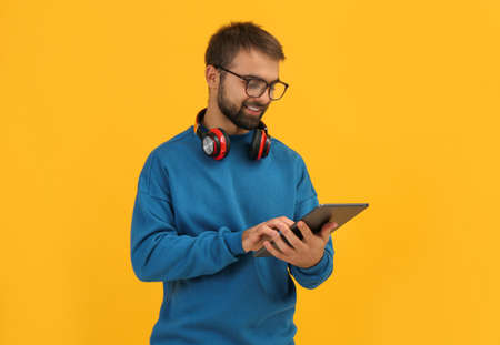 Student with headphones using tablet on yellow background