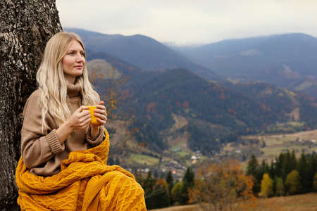 Young woman with mug of hot drink in mountains. Space for textの写真素材