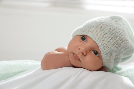 Adorable newborn baby in hat on bed indoors, space for text