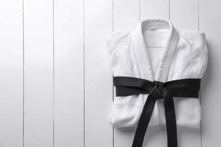 Martial arts uniform with black belt on white wooden background, top view. Space for text