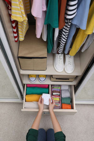 Woman folding clothes in wardrobe drawer indoors, top view. Vertical storageの写真素材