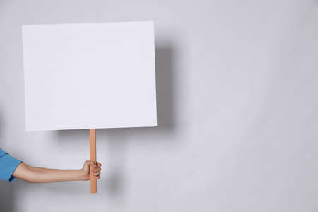 Woman holding blank sign on light gray background, closeup. Space for text