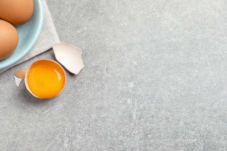 Raw chicken eggs and shell with yolk on light gray table, flat lay. Space for text