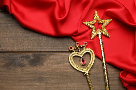 Different golden magic wands and red fabric on wooden table, flat lay. Space for textの写真素材