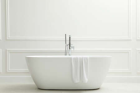 Modern ceramic bathtub with towel near white wall indoorsの写真素材
