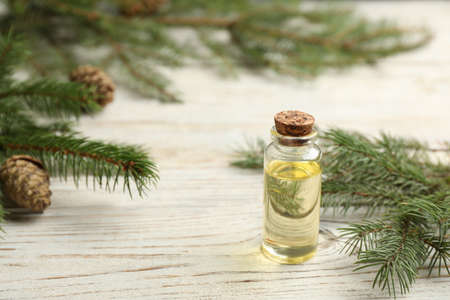Glass bottle of essential oil and fir branches with cones on white wooden tableの写真素材