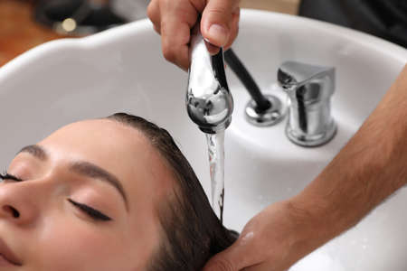 Professional hairdresser washing client's hair at sink indoors, closeupの写真素材