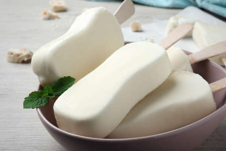 Delicious glazed ice cream bars and mint on white wooden table, closeup
