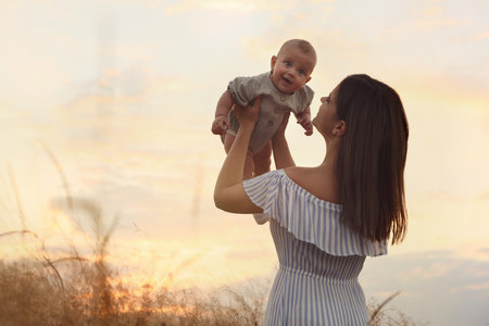 Happy mother with adorable baby in field at sunset, space for textの写真素材
