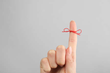 Woman showing index finger with tied red bow as reminder on light gray background, closeup