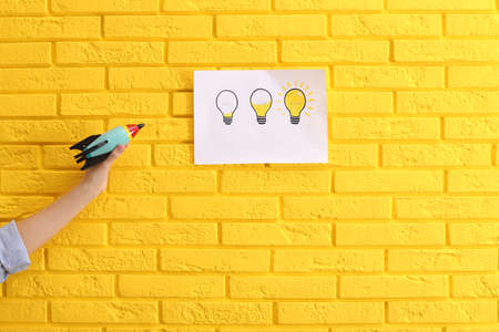 Woman holding toy rocket near yellow brick wall with lamps drawing, closeup. Startup conceptの写真素材