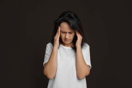 Mature woman suffering from headache on dark brown backgroundの写真素材