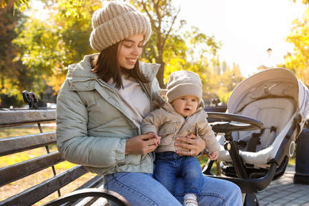 Happy mother with her baby son and stroller in park on autumn day
