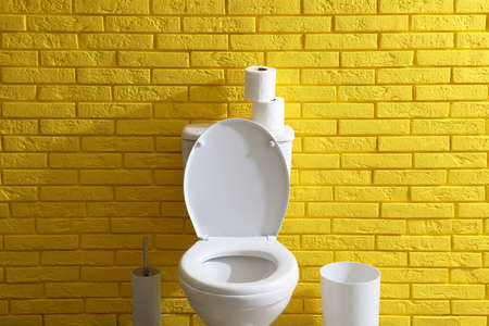 Simple bathroom interior with toilet bowl near yellow brick wall indoors. Home designの写真素材