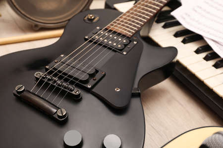Modern electric guitar near other musical instruments on wooden background, closeup