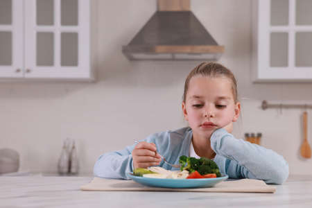 Cute little girl refusing to eat dinner in kitchen, space for textの写真素材