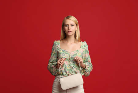 Beautiful stylish woman with trendy baguette bag on red background