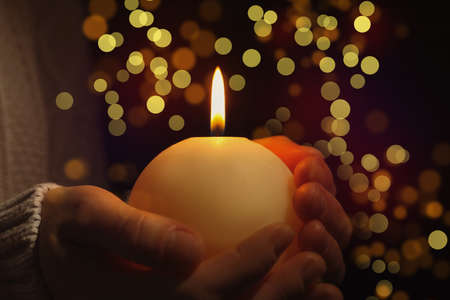 Closeup view of woman holding burning candle in darkness, bokeh effect. Christmas eveの写真素材